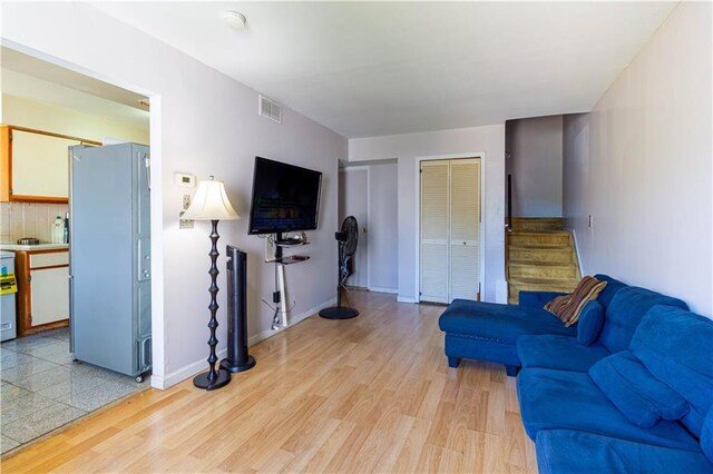 living area with stairway, baseboards, visible vents, and light wood finished floors