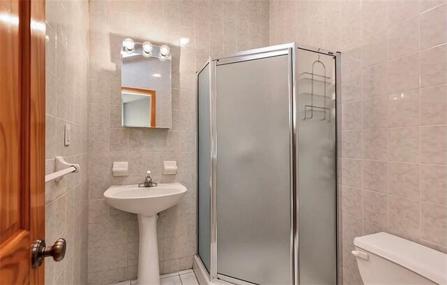 bathroom featuring a shower with door, tile walls, and toilet