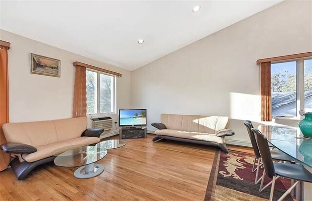 living room with lofted ceiling, hardwood / wood-style floors, a wall mounted air conditioner, and plenty of natural light