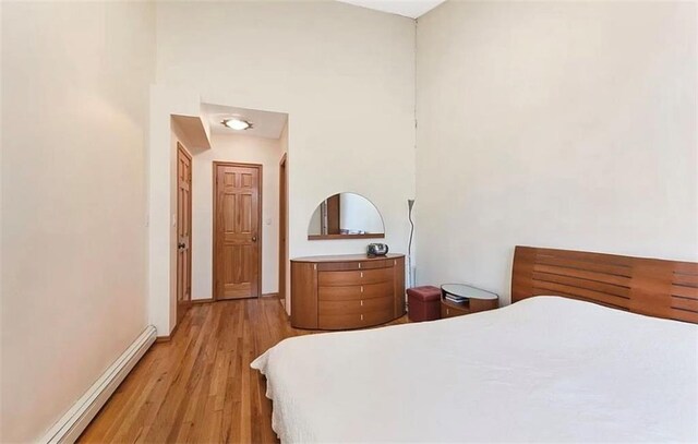 bedroom with a high ceiling, light hardwood / wood-style flooring, and a baseboard heating unit