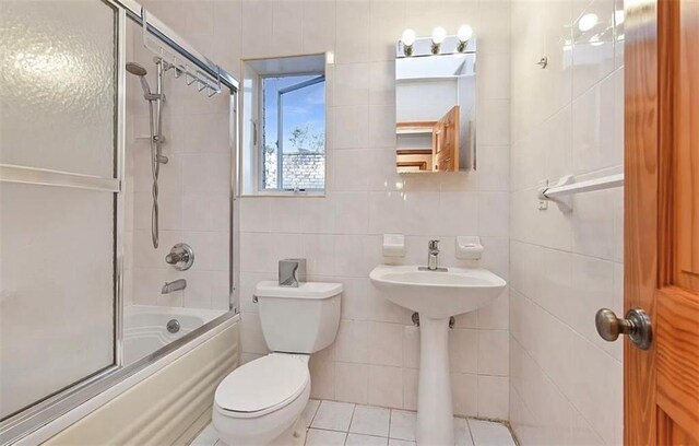 bathroom with tile patterned flooring, tile walls, shower / bath combination with glass door, and toilet