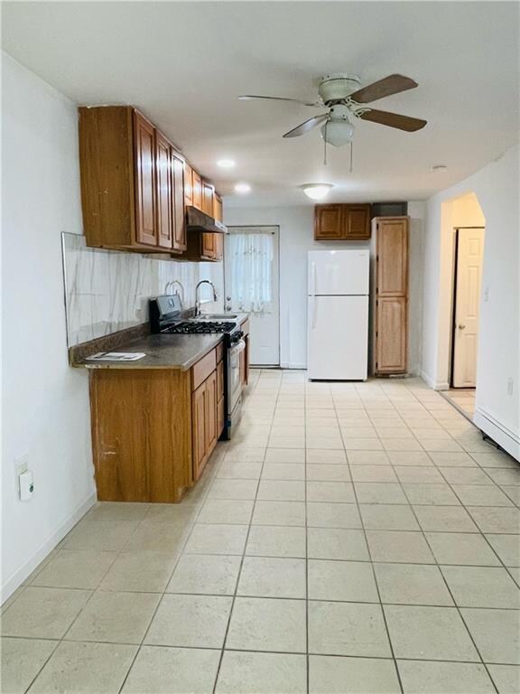 kitchen with light tile patterned floors, stainless steel gas range, ceiling fan, decorative backsplash, and white refrigerator