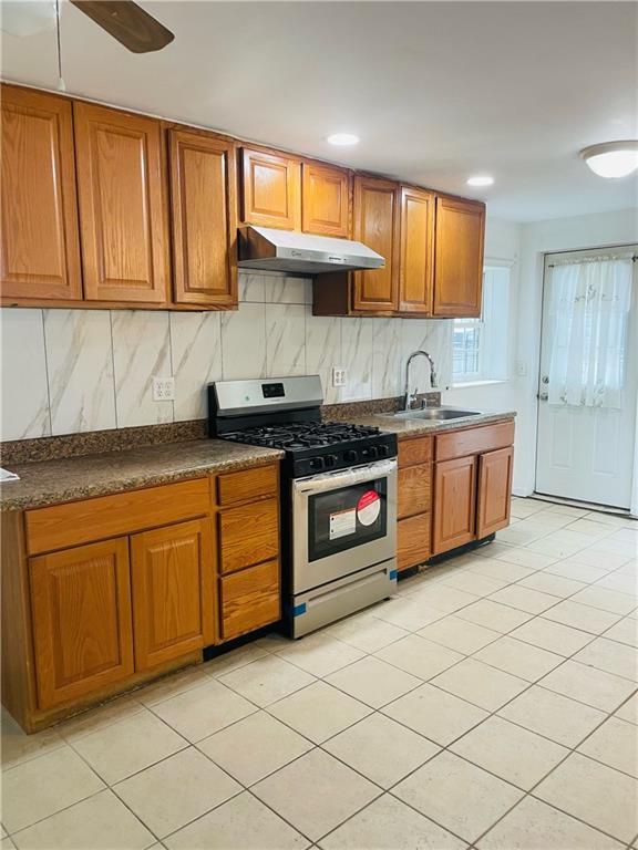 kitchen featuring ceiling fan, decorative backsplash, sink, stainless steel range with gas cooktop, and light tile patterned floors