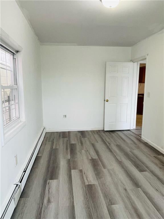 empty room featuring a healthy amount of sunlight, hardwood / wood-style floors, and a baseboard radiator