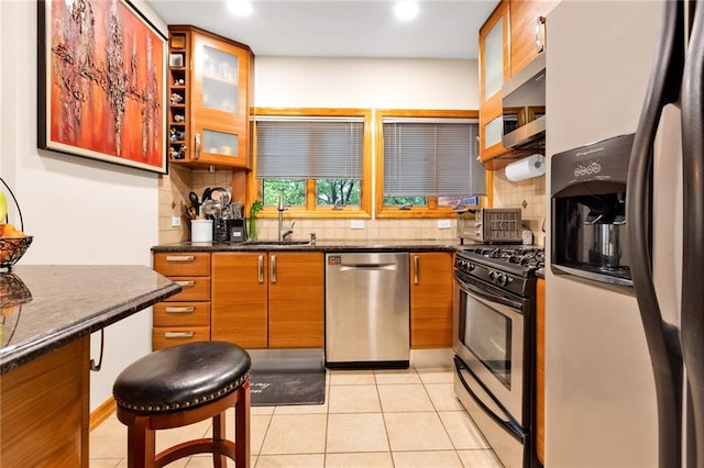 kitchen with brown cabinets, light tile patterned floors, tasteful backsplash, appliances with stainless steel finishes, and a sink