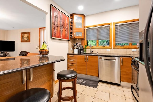 kitchen featuring brown cabinetry, dishwasher, stove, backsplash, and a sink