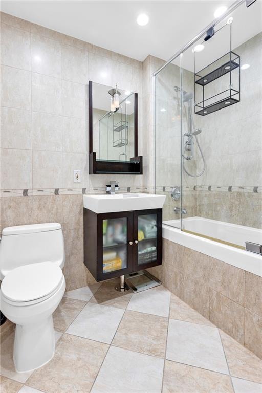 bathroom with tiled shower / bath, tile walls, toilet, vanity, and tile patterned flooring