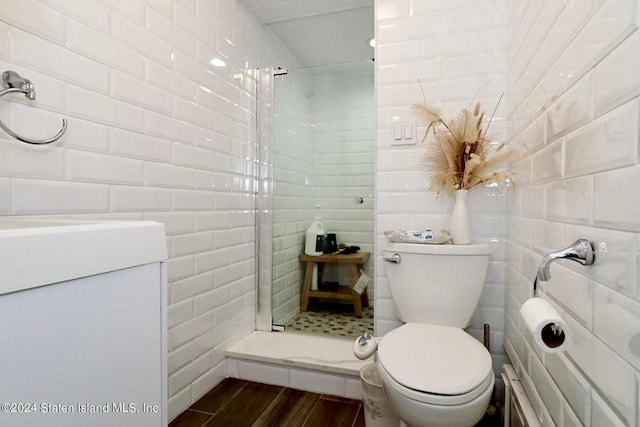 bathroom with a shower stall, tile walls, toilet, and wood finished floors