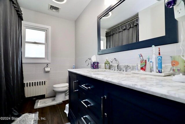 bathroom with hardwood / wood-style floors, radiator heating unit, vanity, tile walls, and toilet