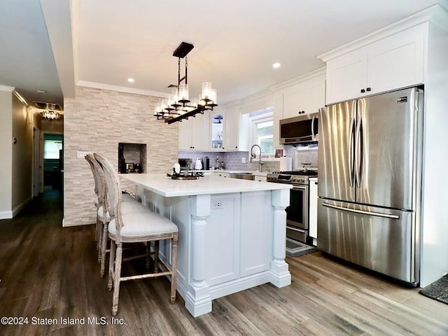 kitchen featuring decorative light fixtures, backsplash, a kitchen island, white cabinetry, and appliances with stainless steel finishes