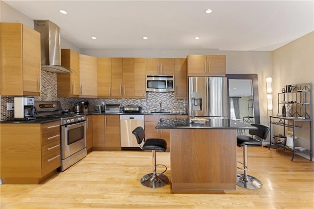 kitchen featuring wall chimney exhaust hood, a breakfast bar area, stainless steel appliances, and a sink