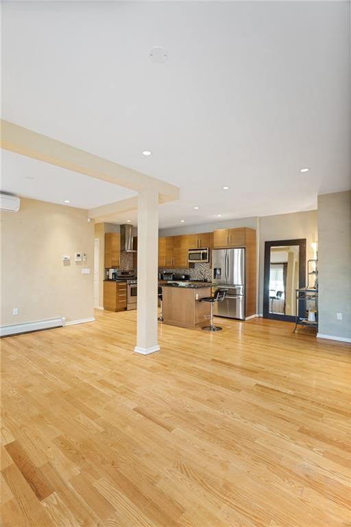 unfurnished living room featuring light hardwood / wood-style floors, a wall mounted AC, and baseboard heating