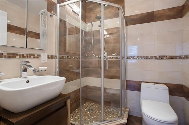 bathroom featuring a shower with door, vanity, tile walls, and toilet