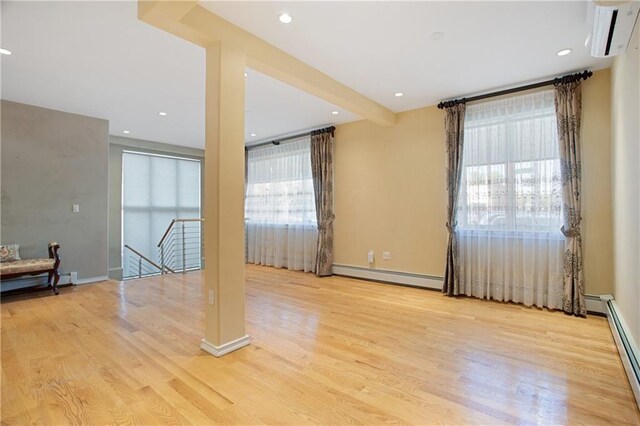 spare room with beamed ceiling, a baseboard radiator, a wall mounted AC, and light wood-type flooring