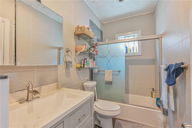 full bathroom with vanity, toilet, tile walls, and bath / shower combo with glass door