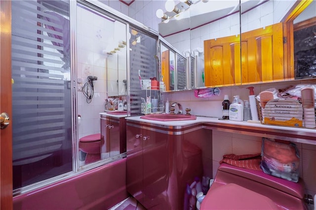 full bathroom featuring backsplash, bath / shower combo with glass door, toilet, vanity, and tile walls