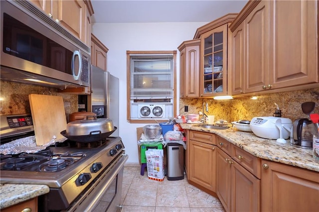 kitchen with backsplash, sink, light tile patterned floors, appliances with stainless steel finishes, and light stone counters