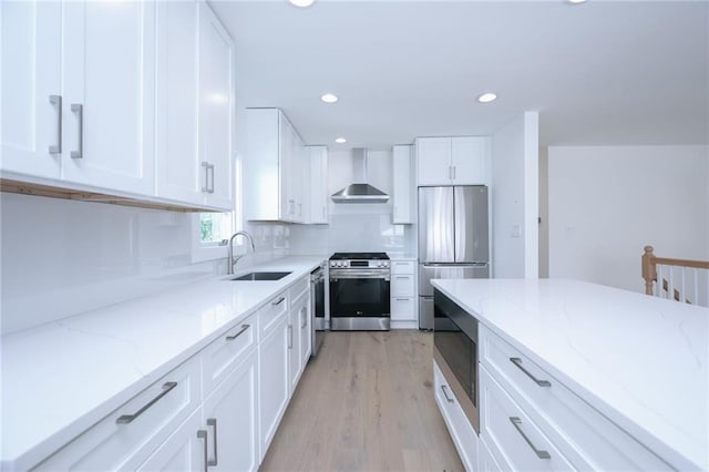 kitchen with white cabinetry, stainless steel appliances, wall chimney range hood, and sink