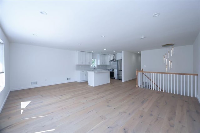 unfurnished living room with sink, a notable chandelier, and light hardwood / wood-style floors