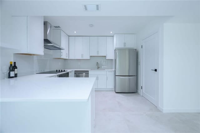 kitchen with wall chimney range hood, kitchen peninsula, white cabinets, appliances with stainless steel finishes, and sink