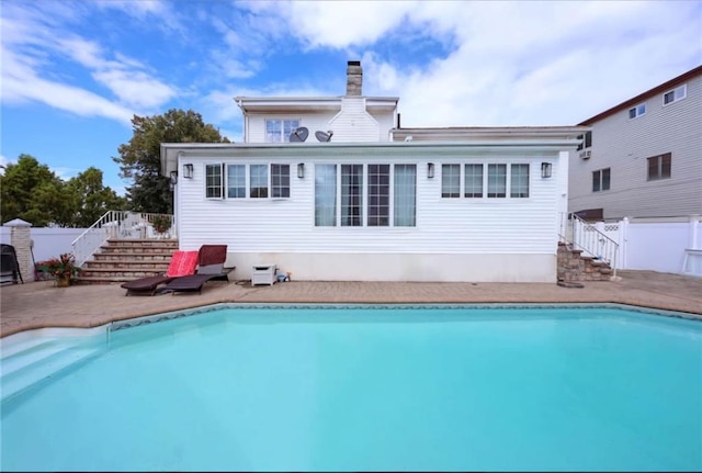 rear view of house featuring fence, stairs, a fenced in pool, a chimney, and a patio area