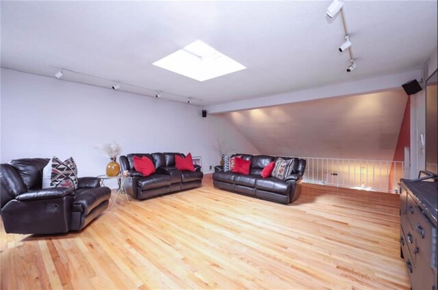 living room featuring rail lighting, vaulted ceiling with skylight, and light hardwood / wood-style floors