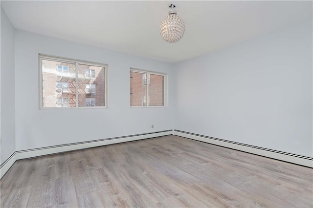 spare room with a notable chandelier, a wealth of natural light, and light hardwood / wood-style floors