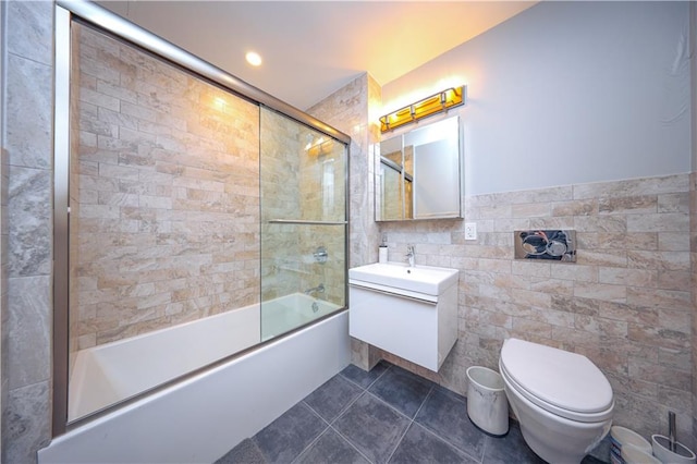 bathroom with toilet, bath / shower combo with glass door, vanity, tile walls, and tile patterned floors