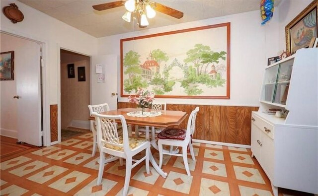 dining space featuring ceiling fan and wood walls