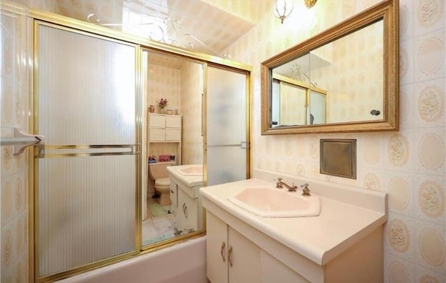 full bath with combined bath / shower with glass door, vanity, toilet, and wallpapered walls