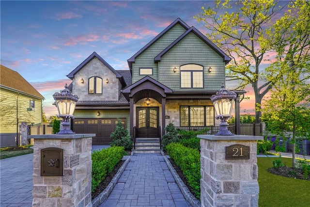 view of front of home featuring decorative driveway, french doors, stone siding, and an attached garage