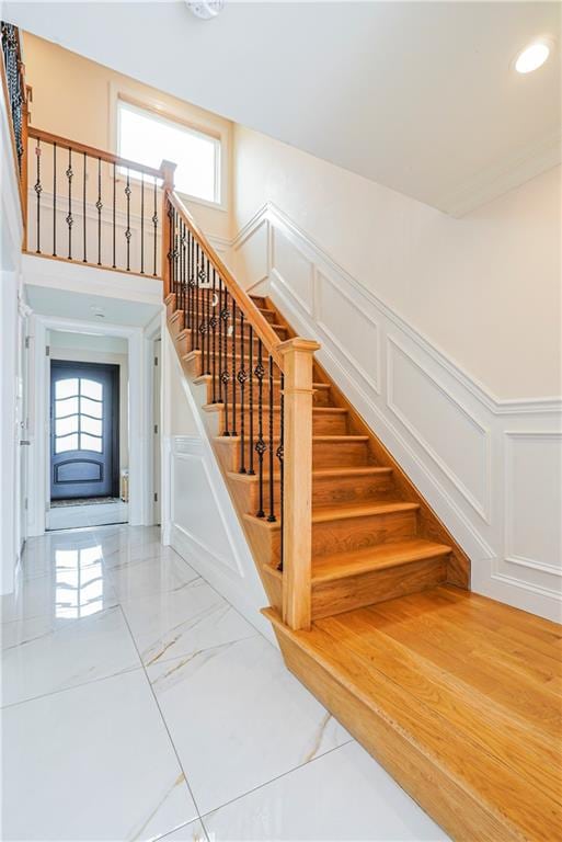 stairs featuring recessed lighting, a wainscoted wall, marble finish floor, and a decorative wall