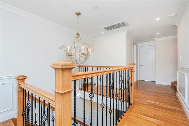 corridor with an upstairs landing, visible vents, light wood-style floors, and ornamental molding