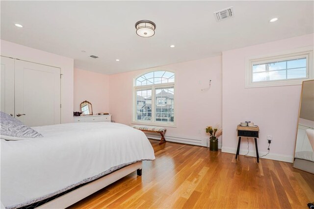 bedroom featuring a baseboard heating unit, light wood-type flooring, and multiple windows