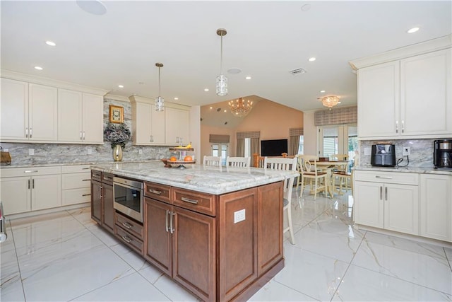 kitchen featuring backsplash, a center island, light stone countertops, hanging light fixtures, and marble finish floor