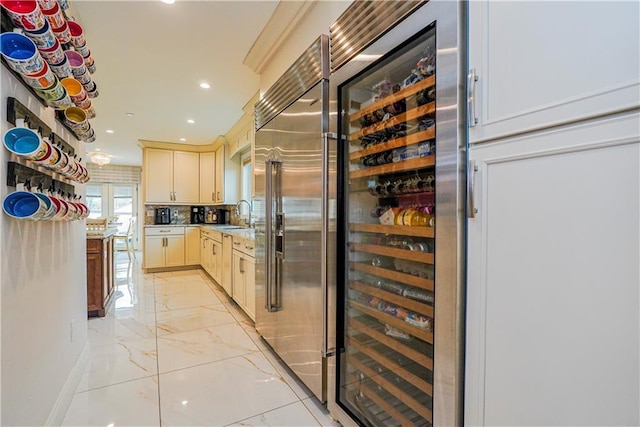 kitchen with wine cooler, stainless steel built in fridge, recessed lighting, marble finish floor, and a sink