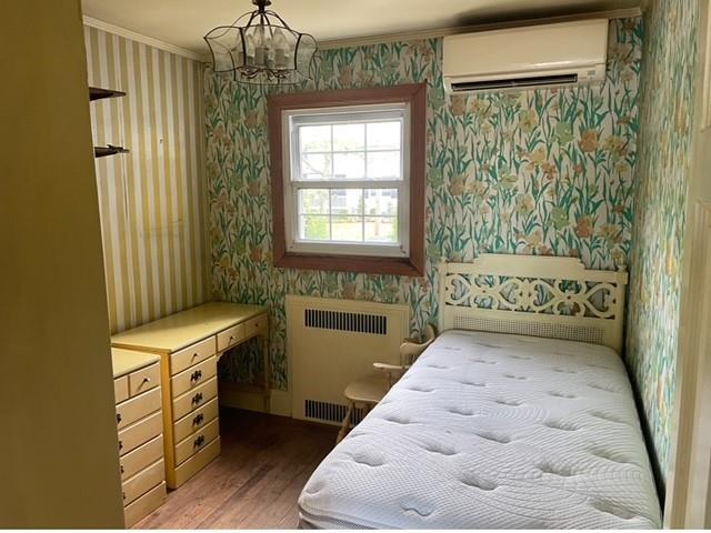 bedroom featuring a wall mounted AC, dark hardwood / wood-style floors, radiator, crown molding, and a chandelier