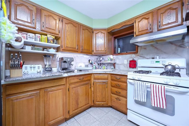 kitchen featuring under cabinet range hood, white gas range oven, brown cabinetry, light countertops, and light tile patterned floors