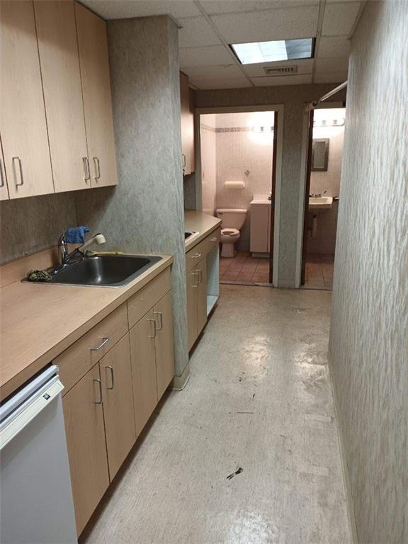 kitchen with light brown cabinetry, sink, dishwasher, washer / clothes dryer, and a drop ceiling