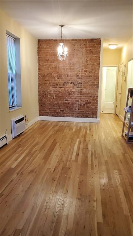 unfurnished dining area with an AC wall unit, brick wall, baseboards, and light wood-style floors