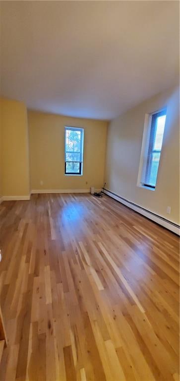 unfurnished room featuring a baseboard radiator, plenty of natural light, and light hardwood / wood-style floors