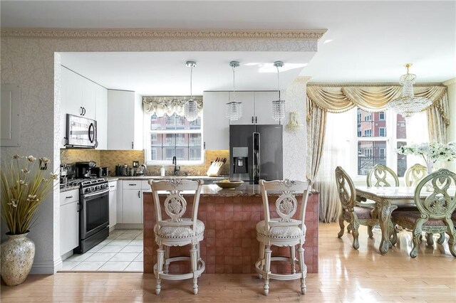 kitchen with a kitchen bar, stainless steel appliances, white cabinetry, and light hardwood / wood-style floors