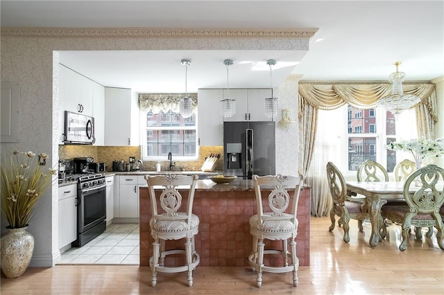 kitchen with stainless steel appliances, a sink, white cabinetry, a kitchen bar, and wallpapered walls