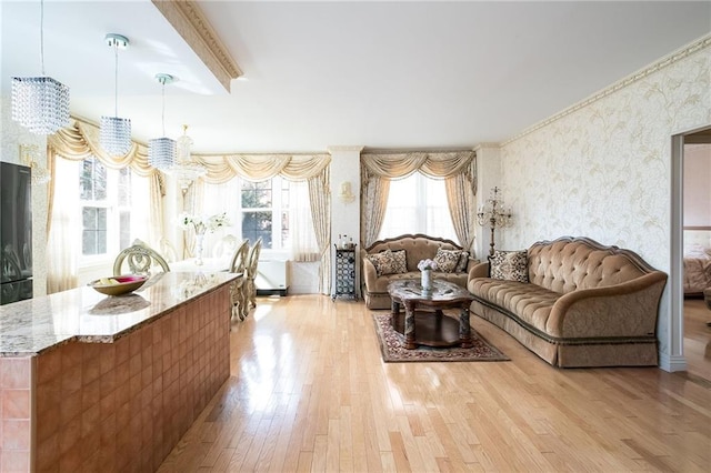 living area featuring wallpapered walls, light wood finished floors, an inviting chandelier, crown molding, and beam ceiling