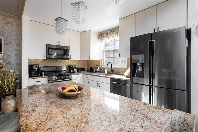 kitchen featuring a sink, hanging light fixtures, appliances with stainless steel finishes, backsplash, and light stone countertops