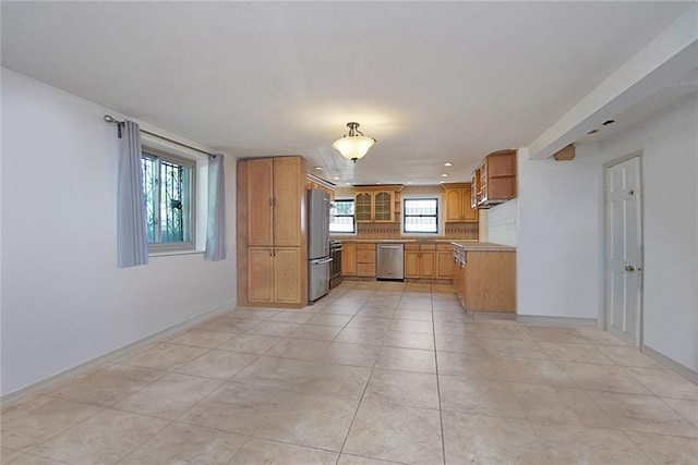 kitchen with light tile patterned floors, baseboards, appliances with stainless steel finishes, brown cabinetry, and glass insert cabinets