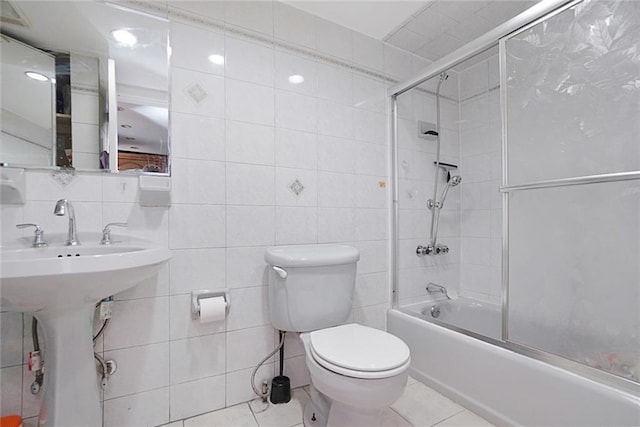 bathroom featuring tasteful backsplash, toilet, shower / bath combination with glass door, tile patterned flooring, and tile walls