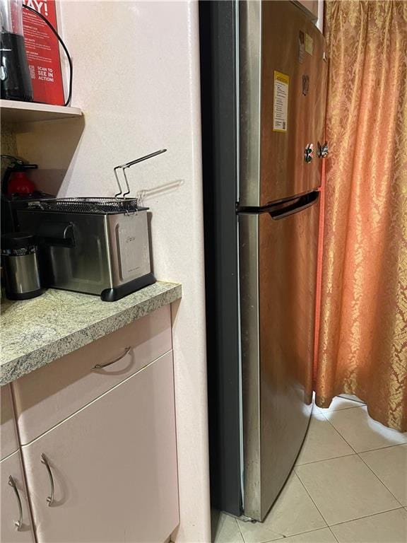 kitchen featuring stainless steel refrigerator, light tile patterned flooring, and light stone countertops