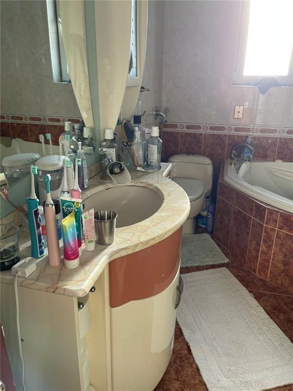 bathroom featuring tiled bath, vanity, tile walls, and toilet