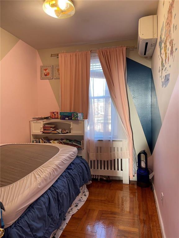 bedroom featuring a wall mounted air conditioner, dark parquet flooring, and radiator heating unit